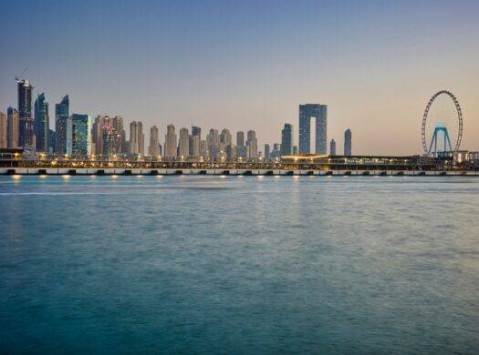 Modern cityscape with skyscrapers and ferris wheel by the water.