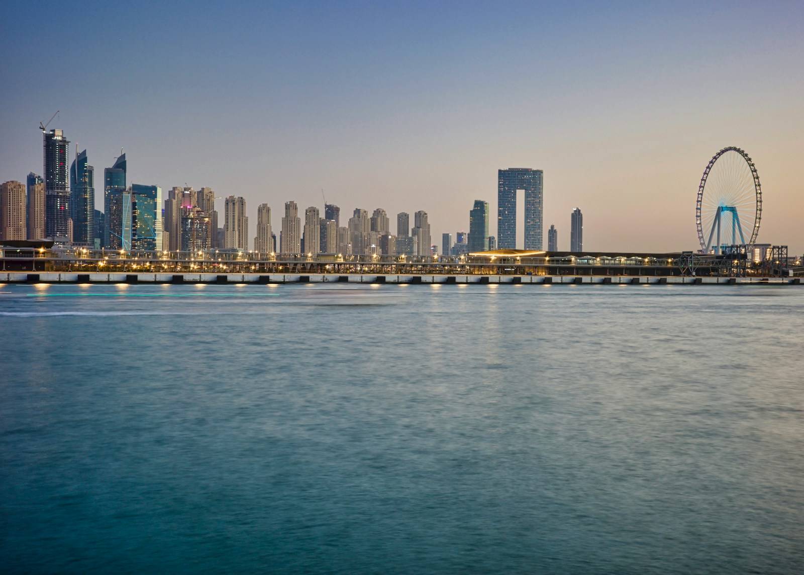 Modern cityscape with skyscrapers and ferris wheel by the water.